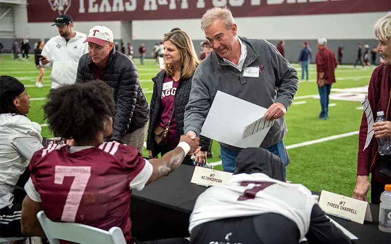 Athletes at table shaking hands with fans