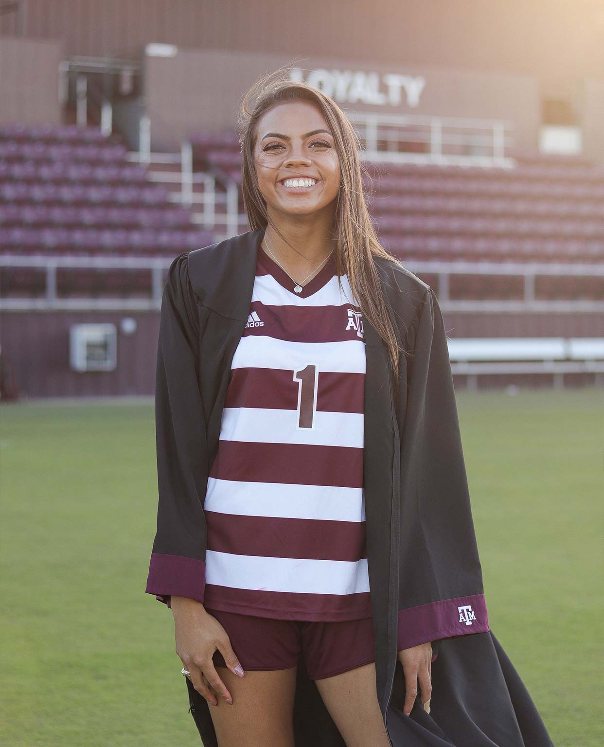 Ally Watt in her graduation gown and soccer uniform posing on the field