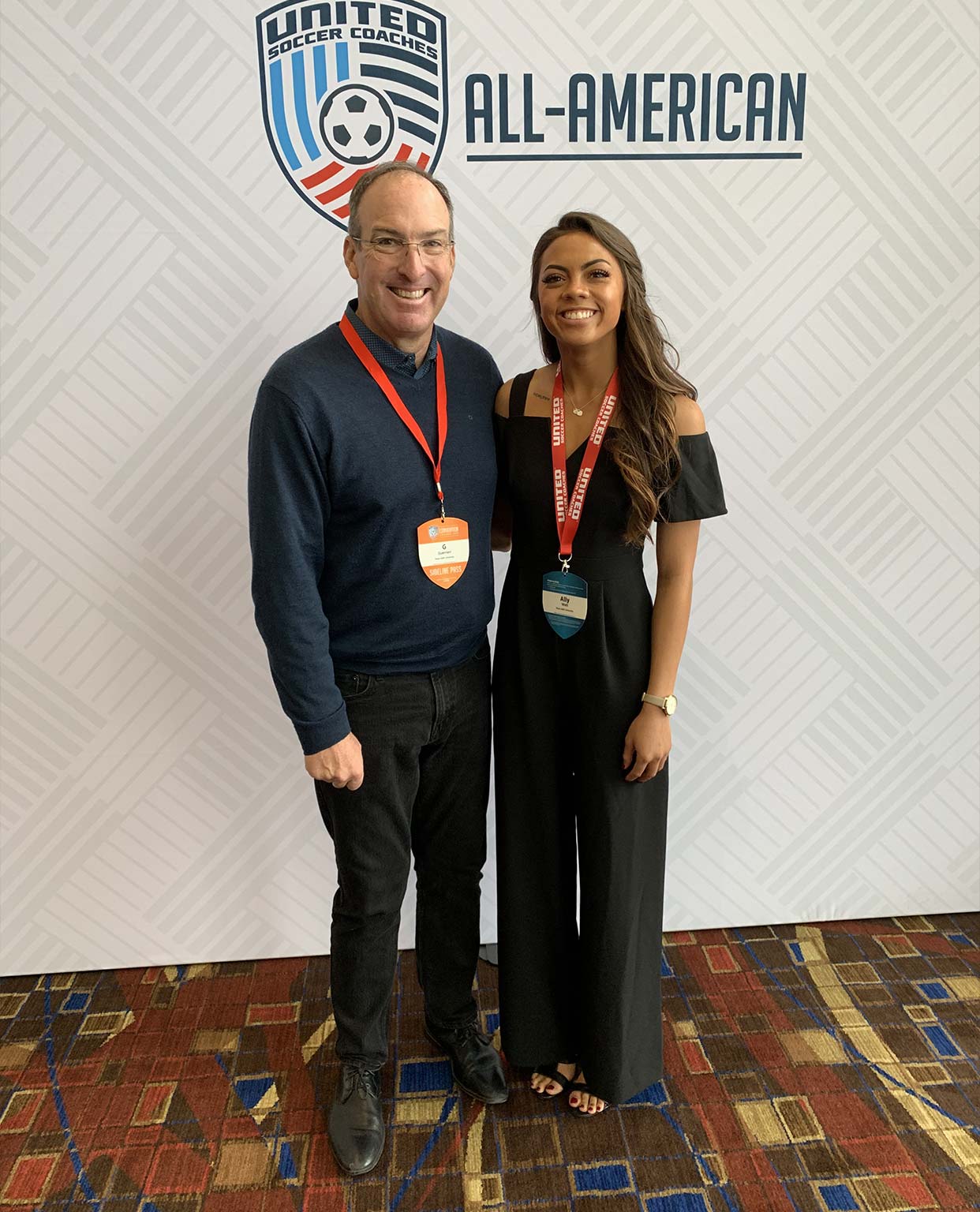 Ally Watt and a gentleman posing in front of a All-American sign