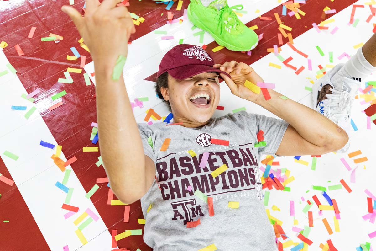 Women's basketball player laying on court with confetti around her smiling
