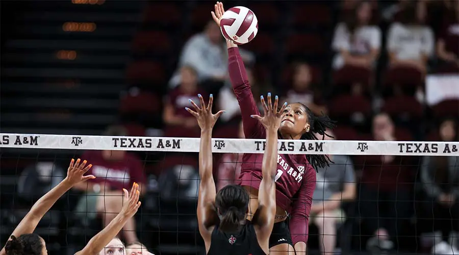 Woman jumping up over net to hit volleyball