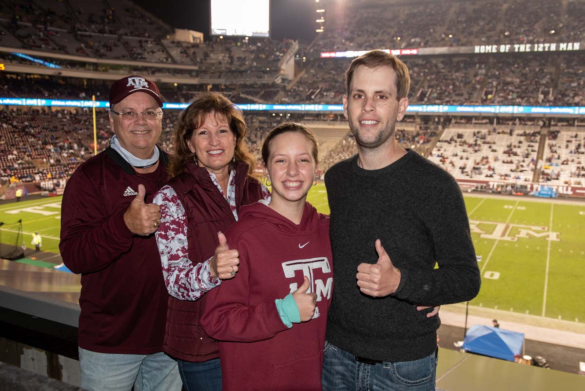 Rhonda & Frosty Gilliam Jr and their family giving thumbs up in front of the football field