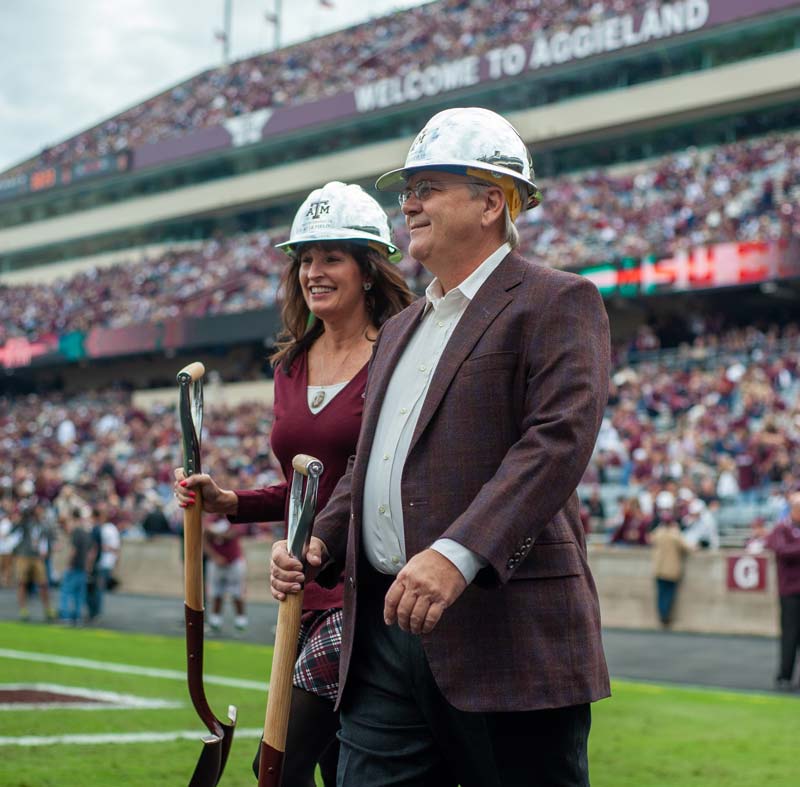 Rhonda & Frosty Gilliam Jr walking onto field with hard hats and shovels