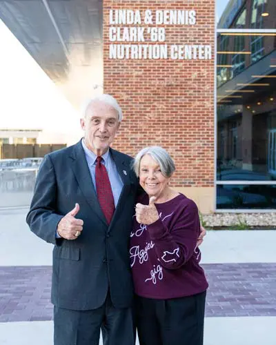 Linda and Dennis Clark standing in front of the Nutrition Center thumbs up
