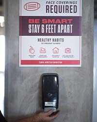 hand sanitizer dispenser underneath 'face mask required' sign