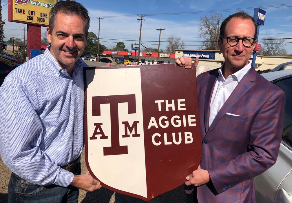 Two men holding a Aggie Club sign